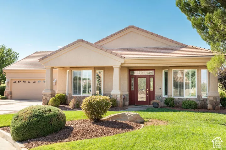 Stucco exterior with stone accents, a tile roof, an attached two-car garage, an ornate red entry door, and a manicured lawn