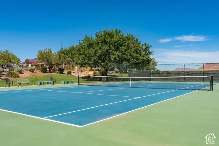 Hard-surface tennis court with blue and green playing areas, perimeter fencing, and mature landscaping