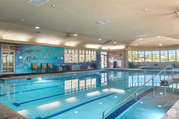 Indoor swimming pool featuring an integrated spa, large windows, and decorative wall mural