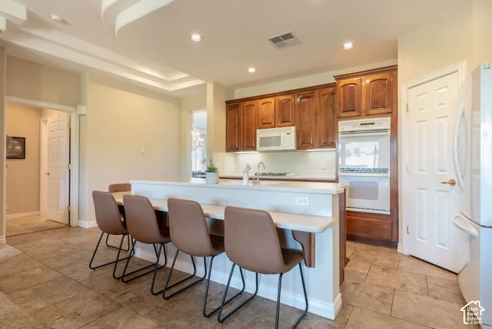 Kitchen featuring wood cabinetry, white appliances, a breakfast bar, recessed lighting, and tile flooring