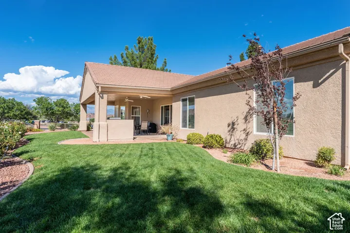 Expansive lawn with mature landscaping, covered patio with outdoor ceiling fans, and stucco exterior