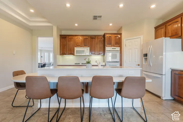 Kitchen featuring wood cabinetry, white appliances, recessed lighting, a tray ceiling, and tile flooring