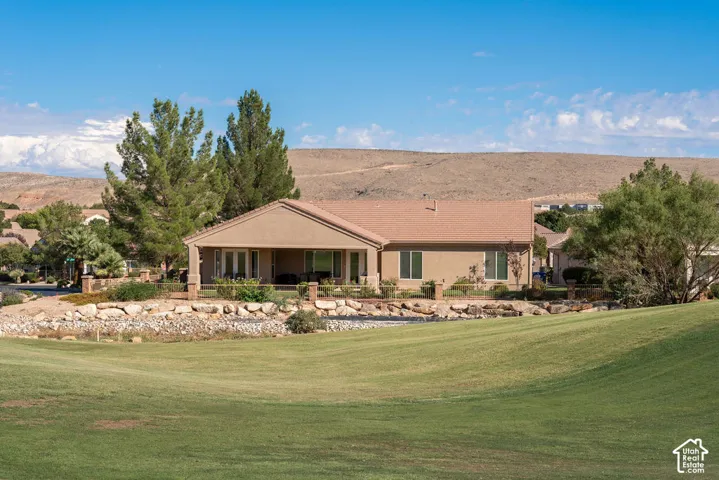 Stucco exterior residence with a covered patio, multiple glass panel doors, and a tiled roof, set against a sloped, manicured lawn with rock landscaping