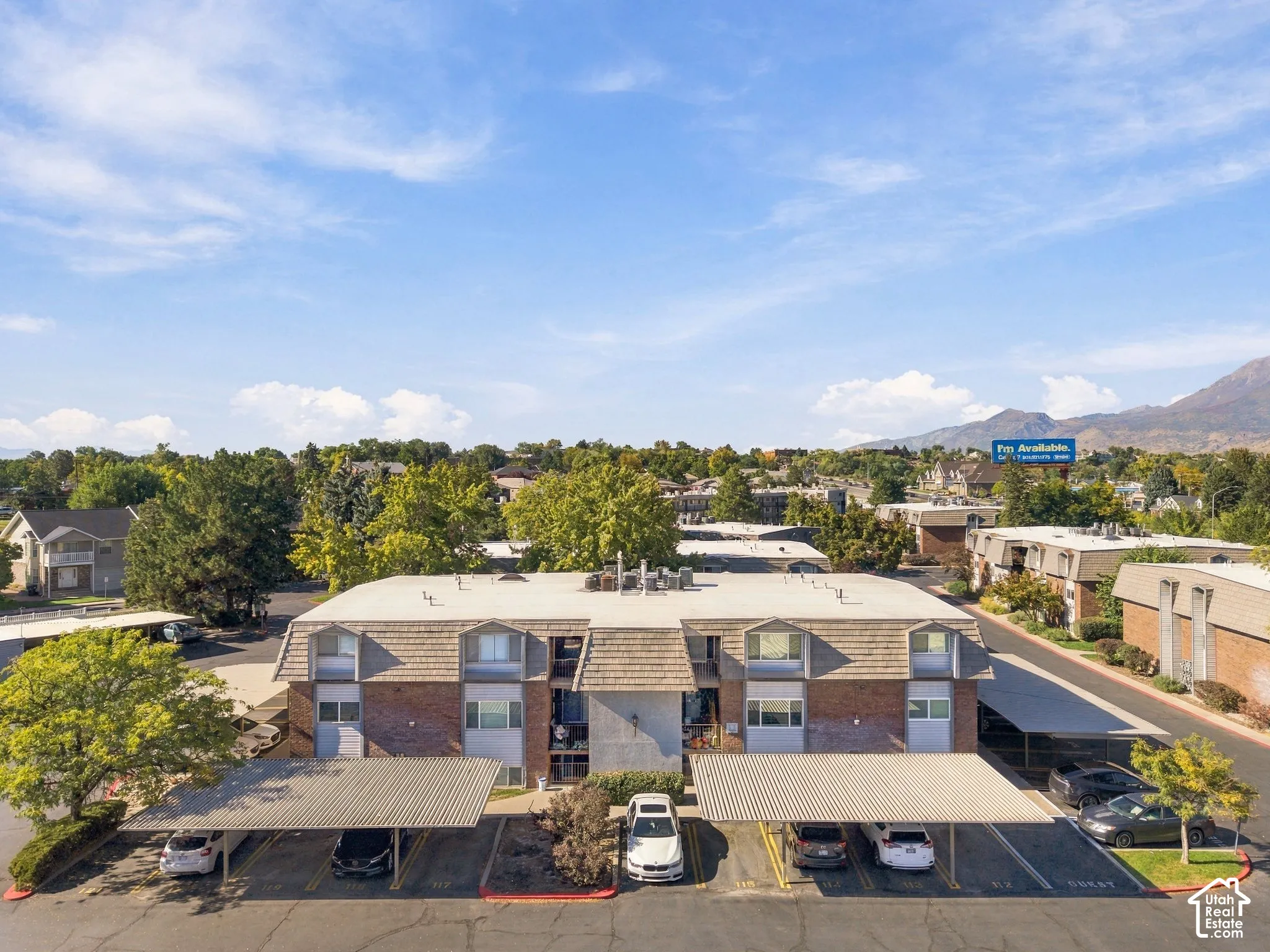 Multi-level structure with brick and siding facade, covered parking areas, mature landscaping, and dormer windows