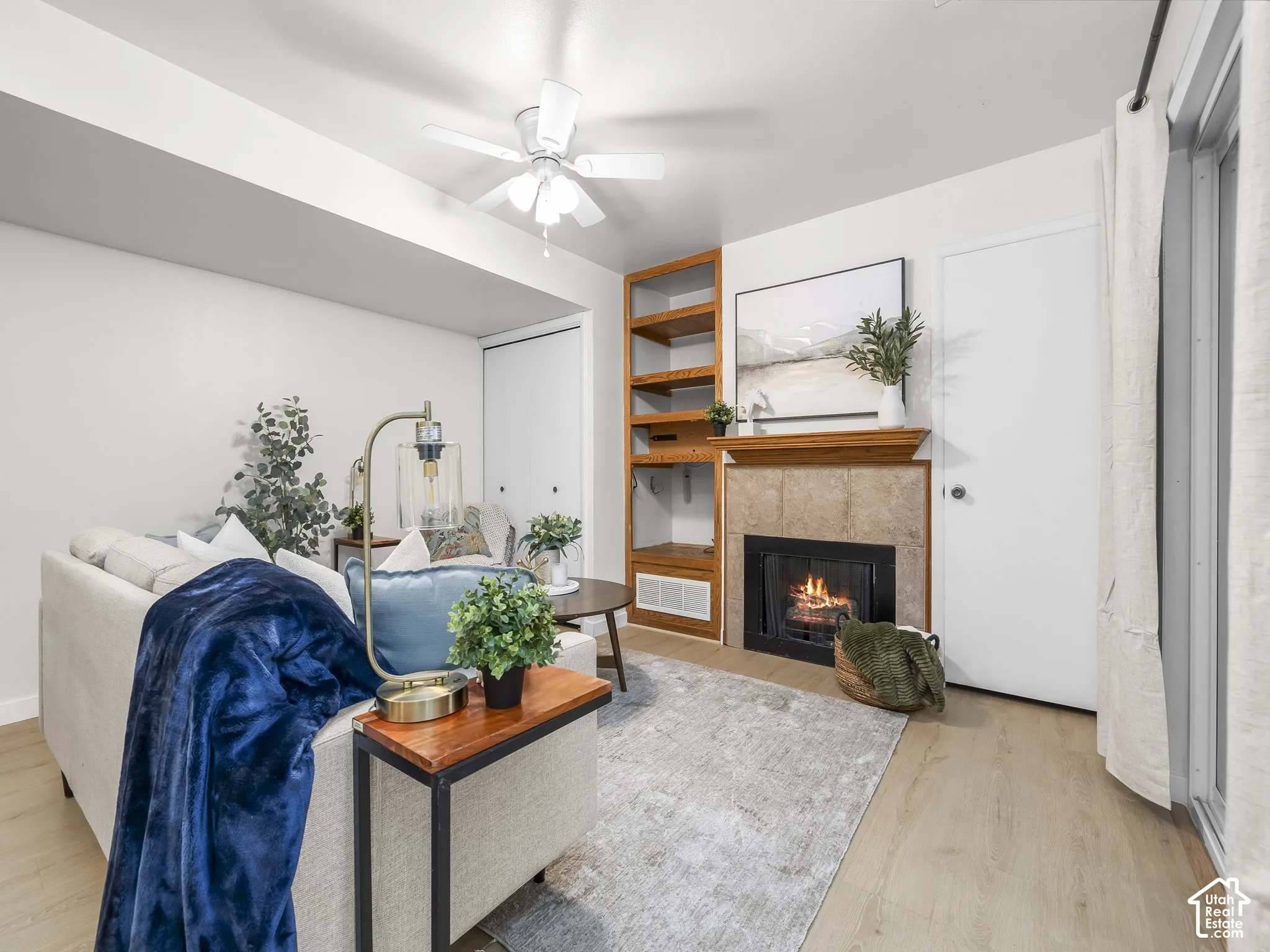 Fireplace with tile surround and wood mantel, built-in shelving, wood-finish flooring, and a ceiling fan