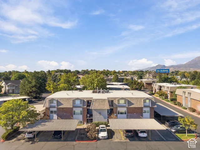 Multi-level structure with brick and siding facade, covered parking areas, mature landscaping, and dormer windows