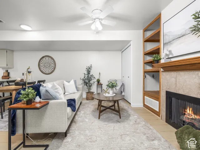Built-in shelving, a tiled fireplace with wood mantel, light wood-finish flooring, and a ceiling fan with integrated lighting