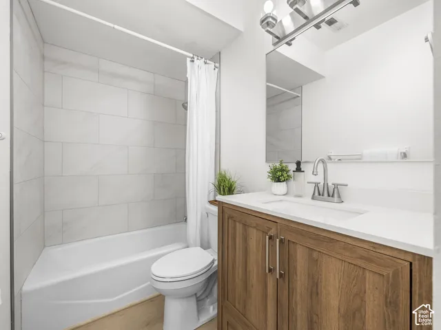 Tub-shower combination with light-toned rectangular wall tiles, wood-finish vanity with dual doors, white countertop with integrated sink, and an overhead vanity light fixture