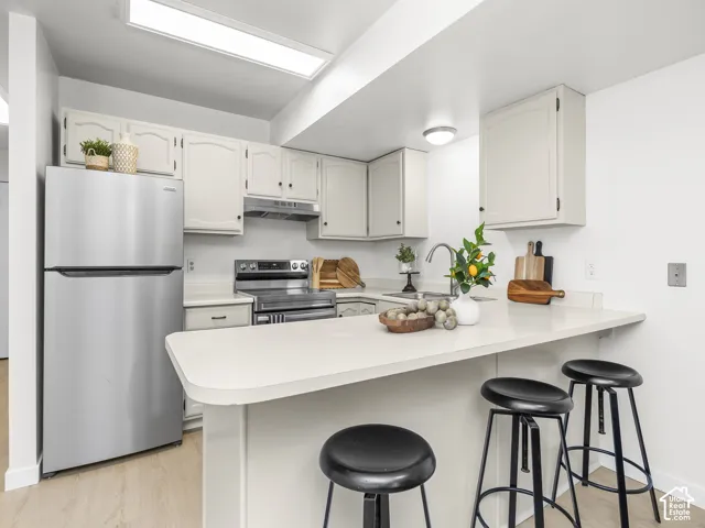 Kitchen featuring light cabinetry, stainless steel appliances, a bar-height counter, a stainless steel sink, and wood-finish flooring