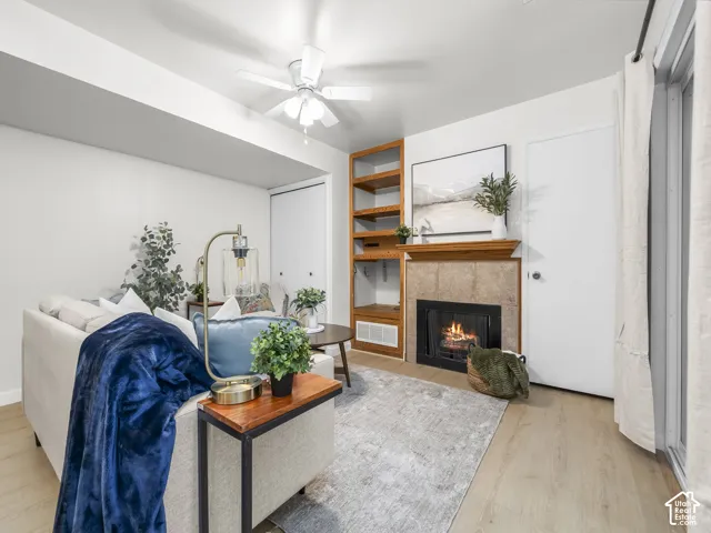 Fireplace with tile surround and wood mantel, built-in shelving, wood-finish flooring, and a ceiling fan
