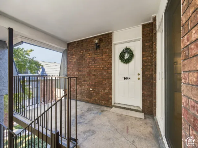 Covered entryway featuring a white door, brick wall, and wrought iron railing