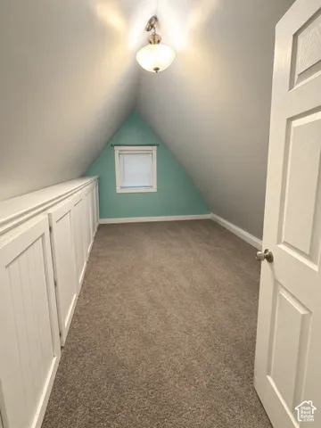 Attic space featuring sloped ceilings, a single window with blinds, recessed built-in cabinetry, and wall-to-wall carpeting