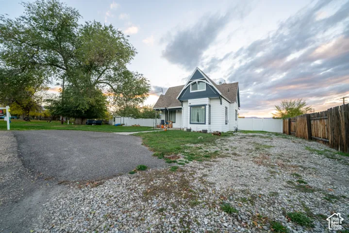 Gabled exterior with clapboard siding, asphalt and gravel driveway, and wood and vinyl perimeter fencing