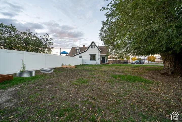 Expansive backyard featuring a white vinyl privacy fence, mature trees, and metal raised garden beds