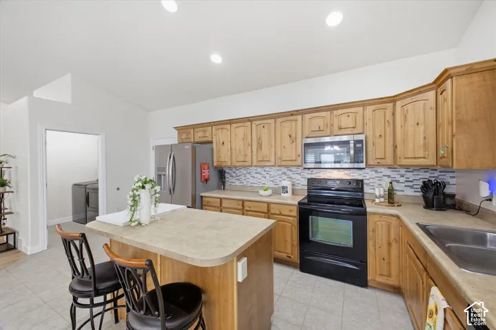 Kitchen featuring light wood cabinetry, a central island, stainless steel appliances, and a tiled backsplash