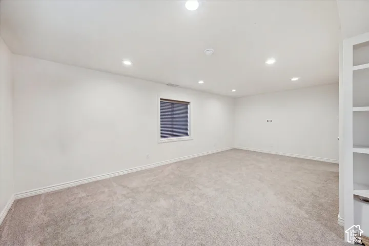 Recessed ceiling lighting, light gray carpeting, window with horizontal blinds, built-in shelving, and white baseboards