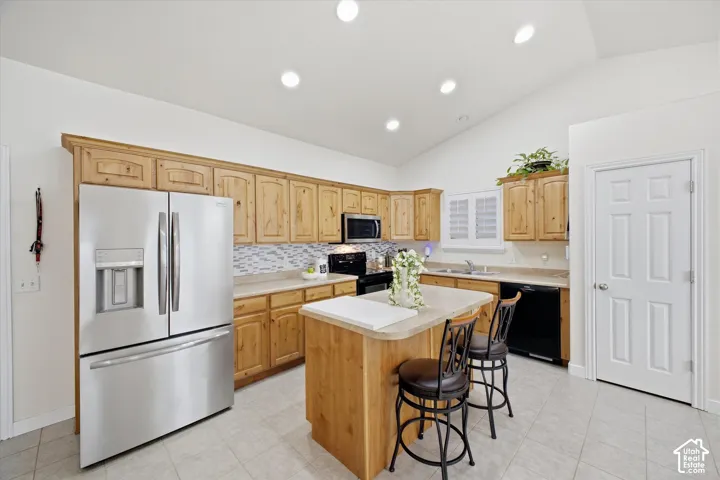Kitchen featuring light wood cabinetry, stone-finish countertops, stainless steel refrigerator, tile backsplash, and vaulted ceiling with recessed lighting