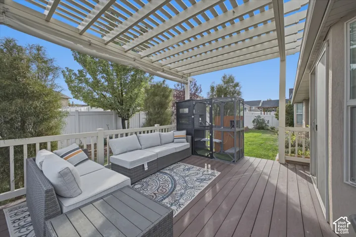 Expansive wood-finish deck with a white slatted pergola, white railing, and a sliding glass door entry. Retractable sun screen