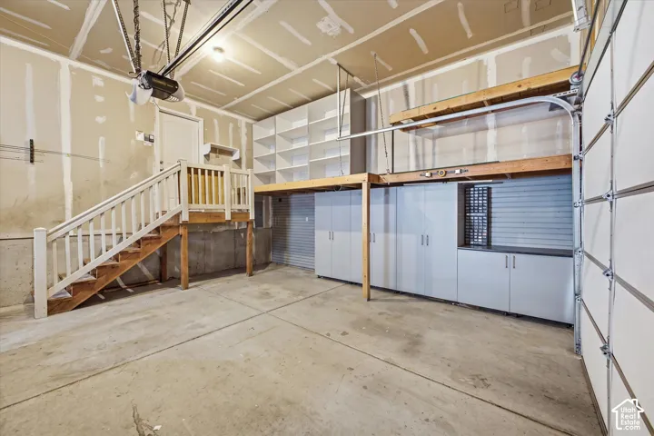 Concrete flooring, built-in cabinetry, slatted wall storage, white shelving, and a wooden staircase with white railings