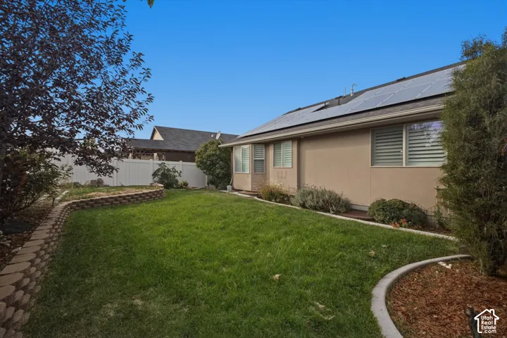 Expansive rear yard with a manicured lawn, established landscaping, and a retaining wall