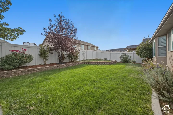 Expansive backyard featuring a lush lawn, white privacy fencing, and a tiered retaining wall with integrated planting beds