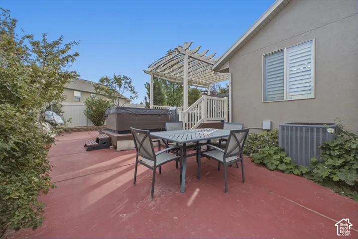 Spacious concrete patio with a hot tub, a pergola, and built-in privacy screening