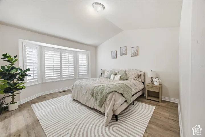 Primary Bedroom. Vaulted ceiling, bay window with plantation shutters, wood-finish flooring, and a recessed light fixture