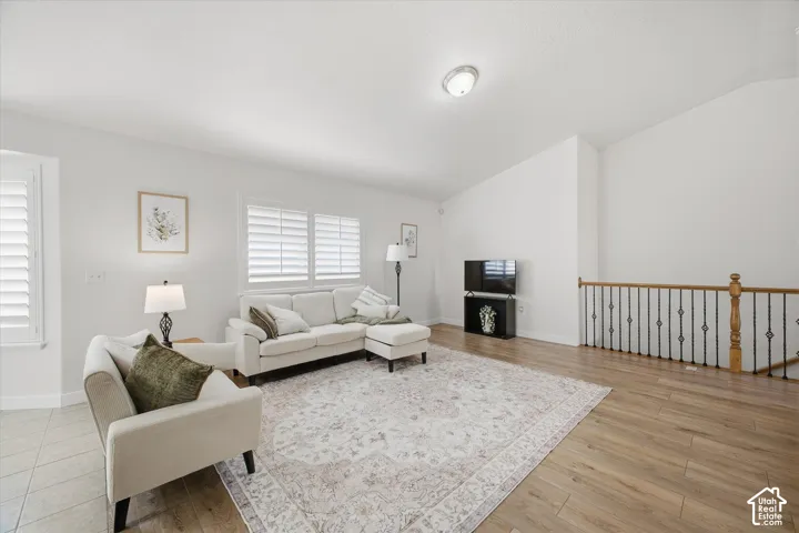 Wood-finish flooring throughout, white walls, vaulted ceiling, white plantation shutters, and a wood and wrought iron railing