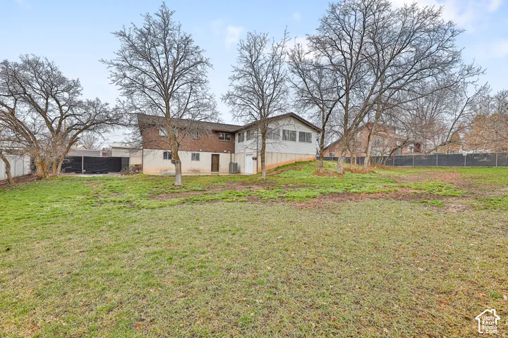 Expansive sloped yard featuring mature trees and a fenced perimeter