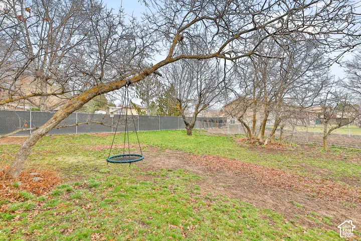 Expansive backyard with a sloped lawn, mature trees, and chain-link fencing