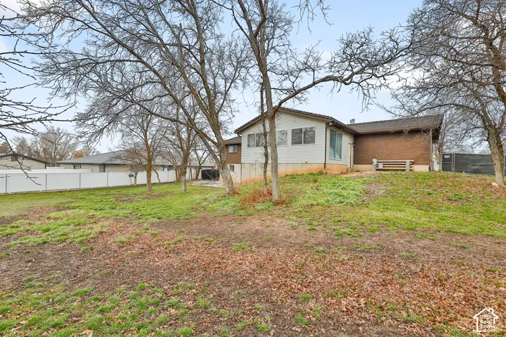 Expansive backyard featuring a sloped lawn and mature trees, with a white vinyl privacy fence and a brick-sided exterior with siding accents