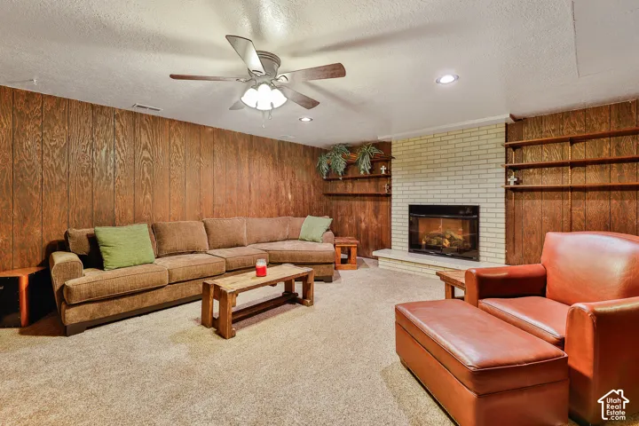Recessed lighting, ceiling fan, fireplace with a brick surround, built-in shelving, wood-paneled walls