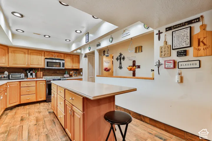 Kitchen featuring wood-finish flooring, recessed lighting, wood cabinetry, and a center island with a light-toned countertop