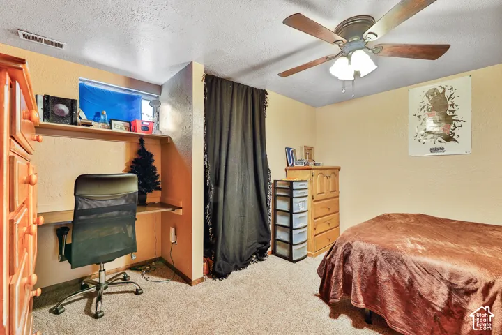 Built-in desk with shelving, wood-finish ceiling fan, and light-toned carpet flooring