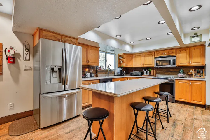 Kitchen featuring a central island, wood-finish flooring, stainless steel appliances, recessed lighting, and ample cabinetry