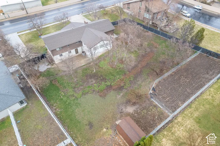 Expansive property featuring a large structure, patio area, cultivated garden bed, storage shed, and perimeter fencing