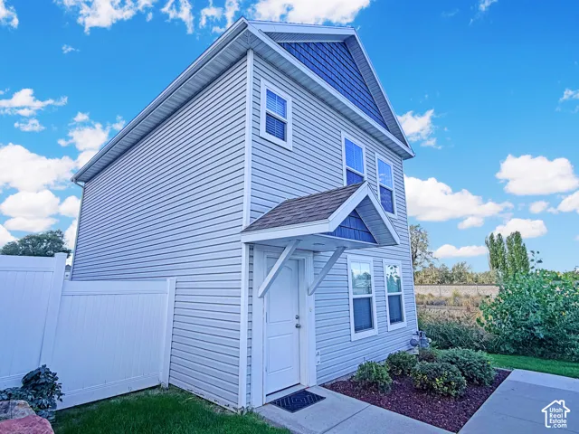 Two-story exterior featuring light-colored siding, contrasting blue shingle accents, a covered entry, multiple windows, and a paved walkway