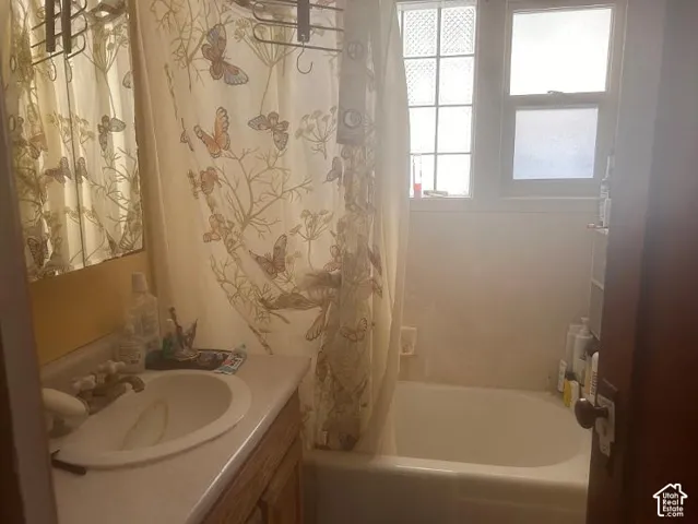 Built-in bathtub, dual windows with privacy glass, vanity with integrated sink, and wood-finish cabinetry