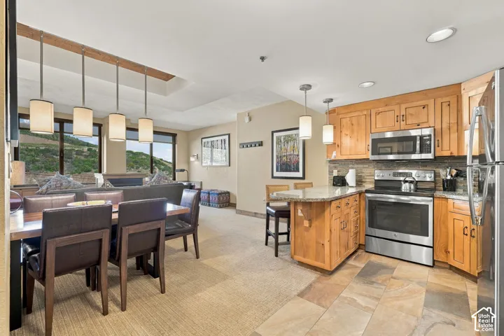Open-concept living area featuring distinct kitchen and dining zones, wood cabinetry, stainless steel appliances, and large windows