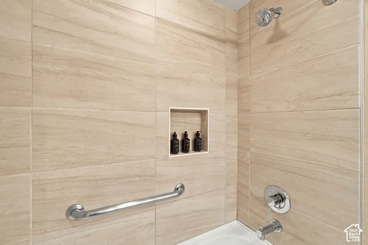 Bathtub and shower combination with beige-toned tile surround, recessed niche, chrome shower head, and chrome grab bar