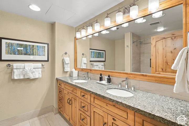 Dual vanity with granite countertop, wood-finish cabinetry, and framed mirror