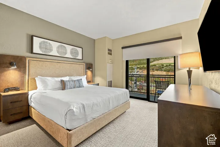Wall-mounted bedside lighting fixtures, built-in headboard with integrated nightstands, full-length sliding glass doors, private balcony with metal railings, and carpeted flooring