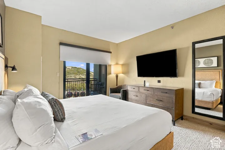 Wood-finish flooring, a wall-mounted television, a large full-length mirror, a built-in dresser, and an exterior balcony with a metal railing