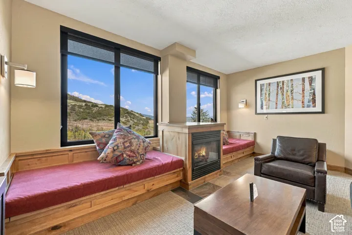 Built-in wooden bench seating, wall-mounted light fixtures, natural stone flooring surrounding the fireplace, and dual windows with mountain scenery