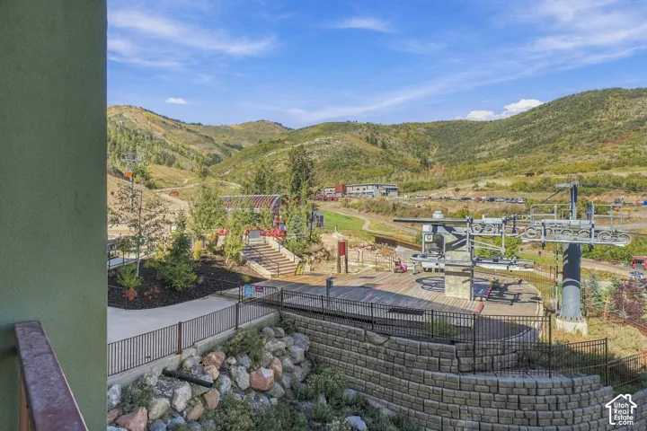 Mountainous landscape backdrop, ski lift infrastructure, stone retaining wall, paved pathways, and landscaped plantings