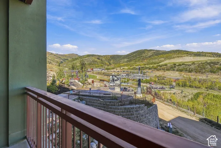 Balcony with metal railing, overlooking hillside terrain with a ski lift structure, and a retaining wall of stacked stone