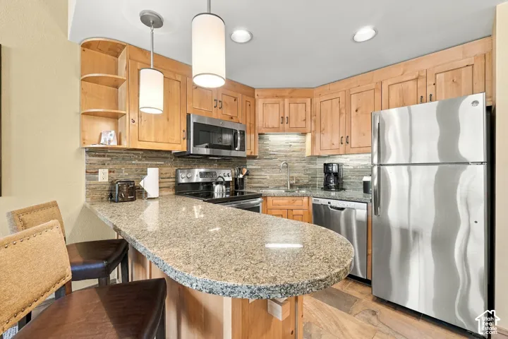 Kitchen featuring wood cabinetry, stainless steel appliances, a stone tile backsplash, a curved breakfast bar, and recessed lighting