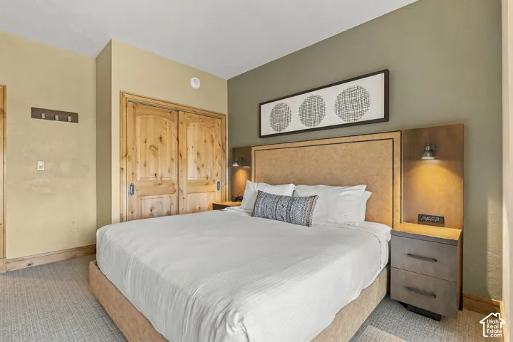 Integrated wall-mounted sconce lighting, built-in headboard, wood-finish sliding closet doors, built-in bedside table with two drawers, and carpeted flooring