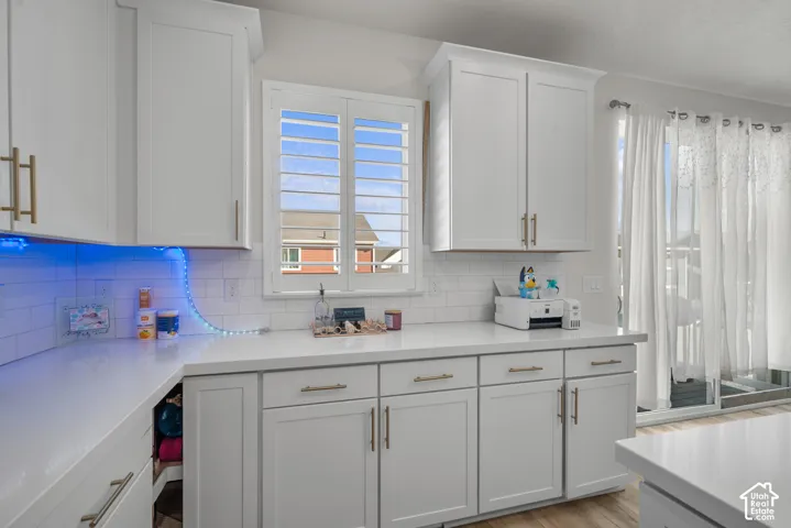White shaker cabinetry with gold-tone hardware, white countertops, subway tile backsplash, window with plantation shutters, and sliding glass door