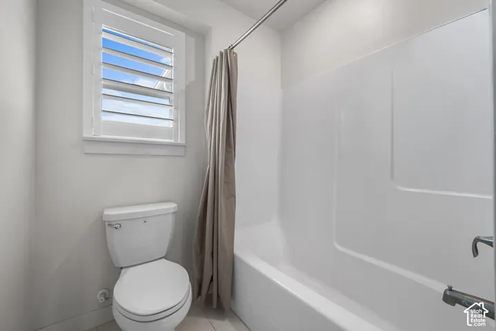 White tub and shower combination with a white toilet and window featuring horizontal louvered shutters